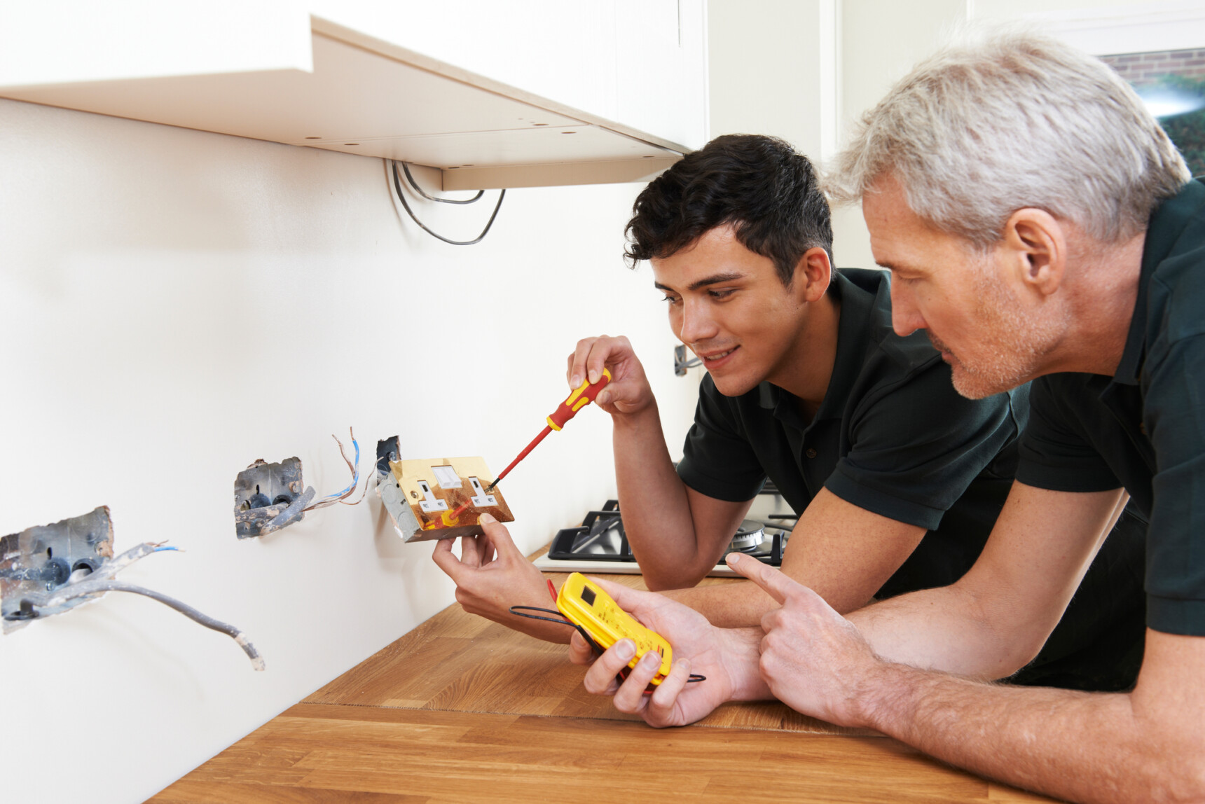 A male apprentice working with an electrician in a new house.