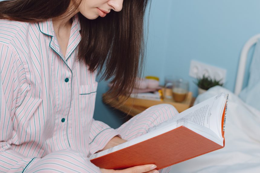 A teenage girl wearing pyjamas is reading a book in bed the night before an exam.