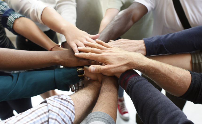 Diverse team of people placing their hands on one another.
