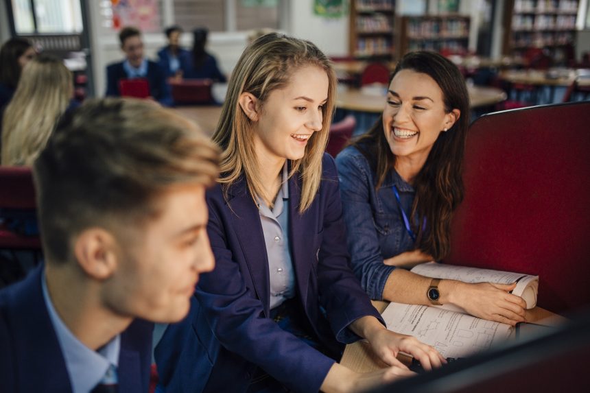 A male and female student working at a computer alongside their smiling teacher.