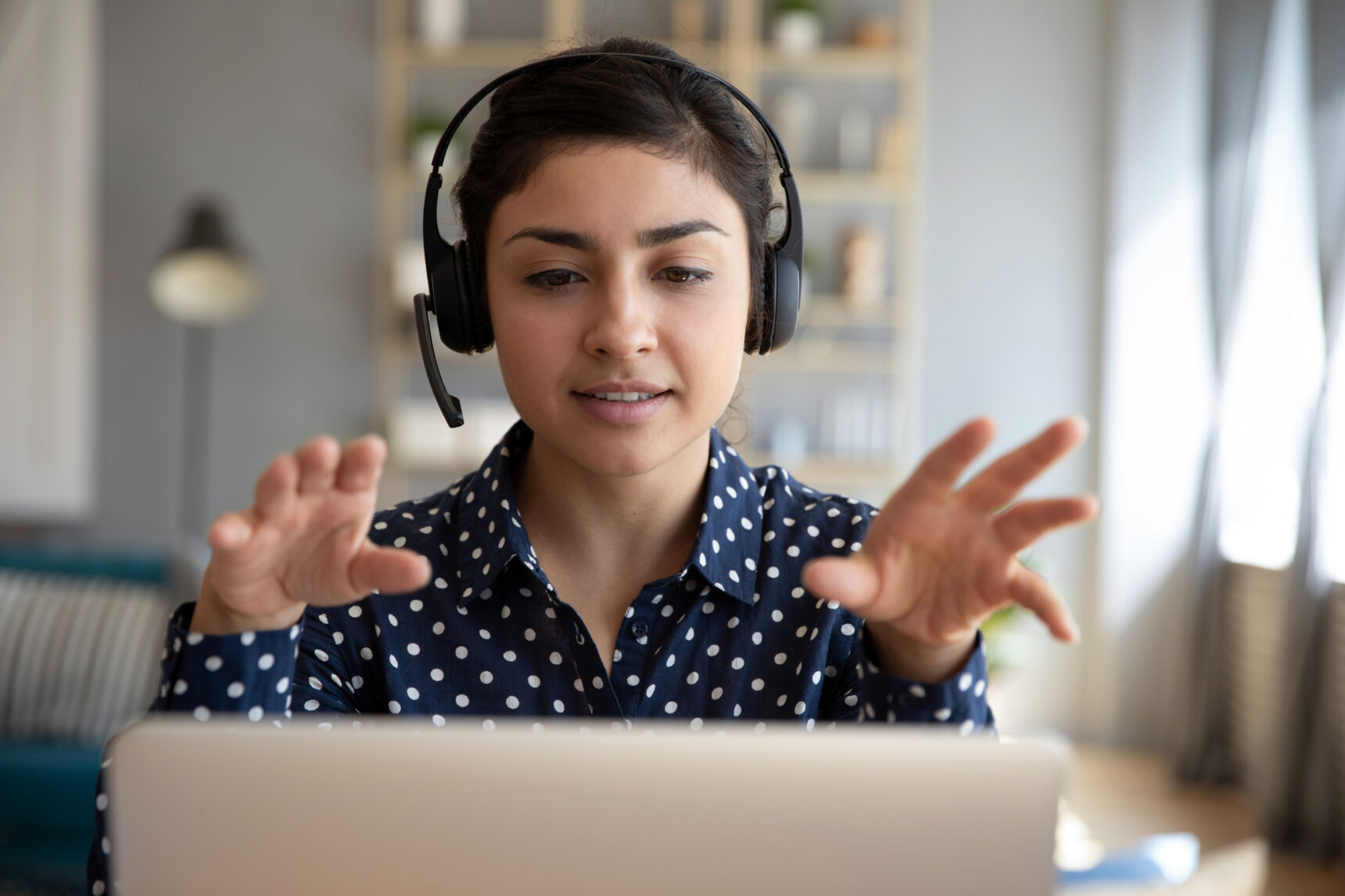 A female online tutor teaching using a laptop, headphones, and microphone.