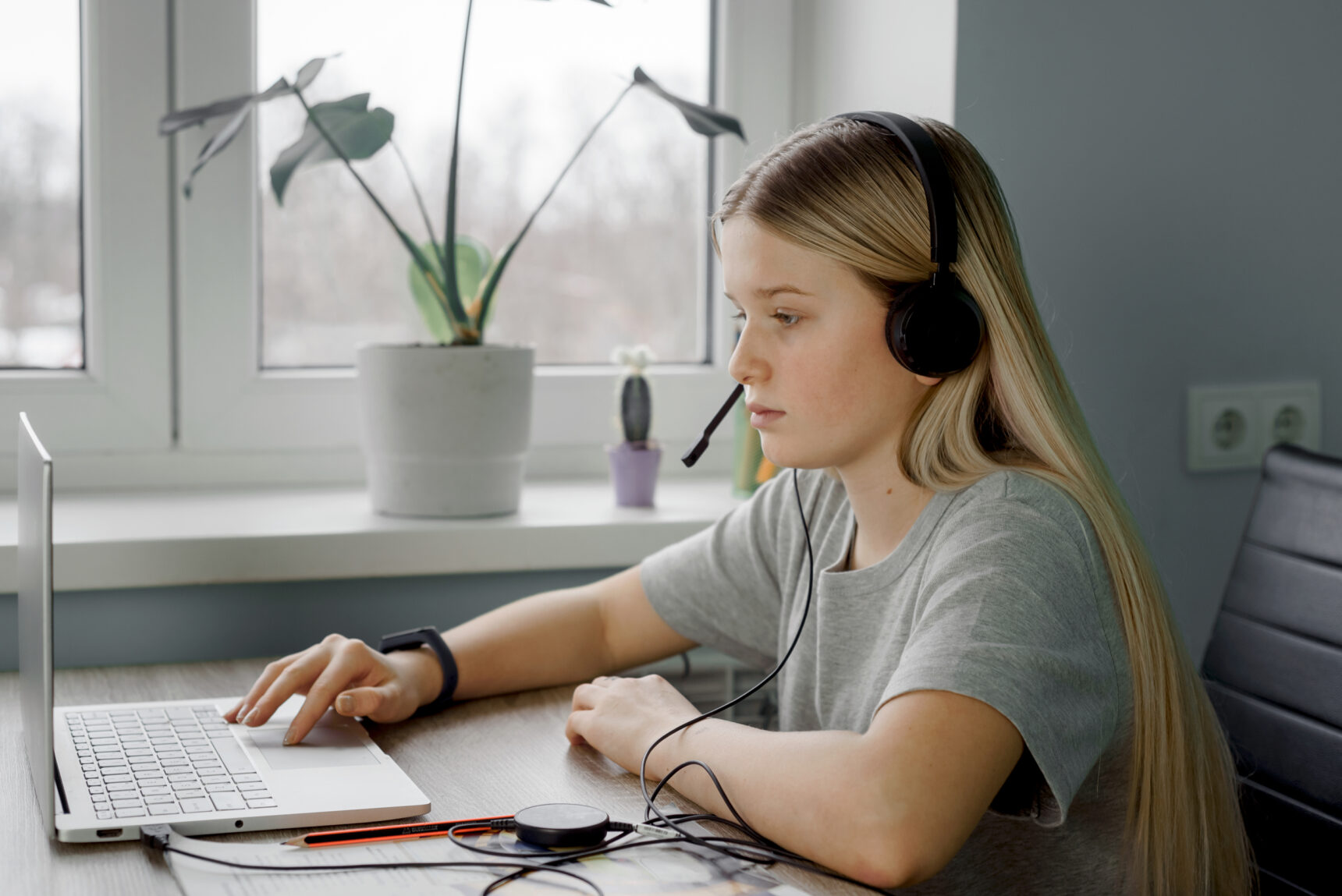 A girl is working on a computer in a tidy and uncluttered study space filled with natural light from a window.