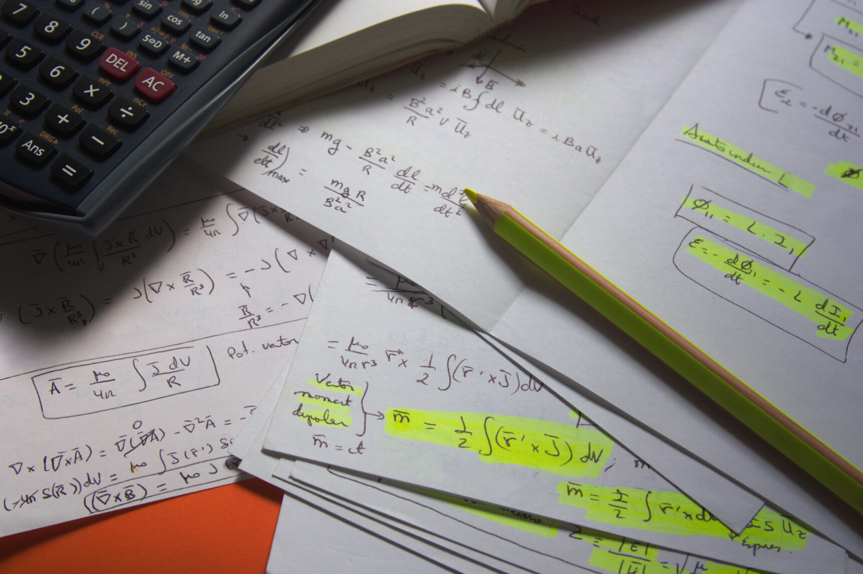 A calculator and a stack of papers featuring physics formulae, some of which are highlighted in yellow.