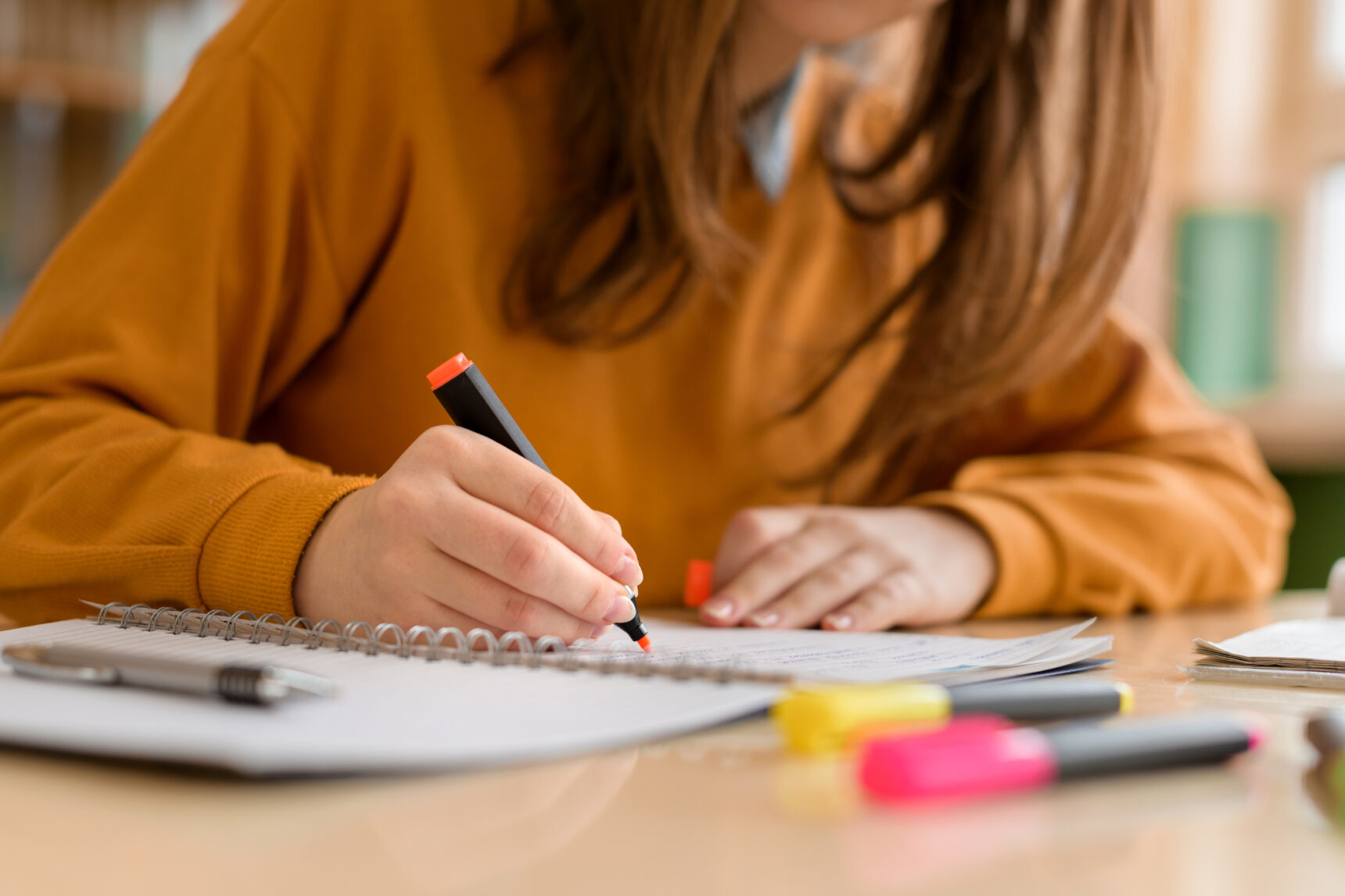 A teenage girl sits at a desk highlighting notes as she revises for GCSE Geography Paper 3.