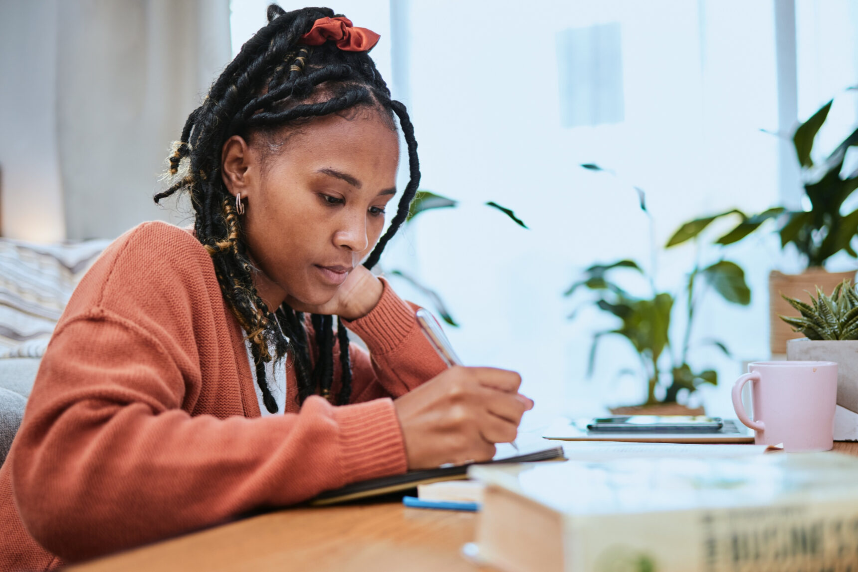 A female GCSE student sits at a desk writing as she studies for the AQA Geography Paper 3 exam.