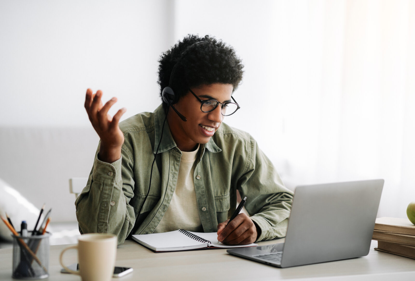 A male online tutor sits at a desk in front of his laptop, asking his student for a tutor review at the end of a lesson.