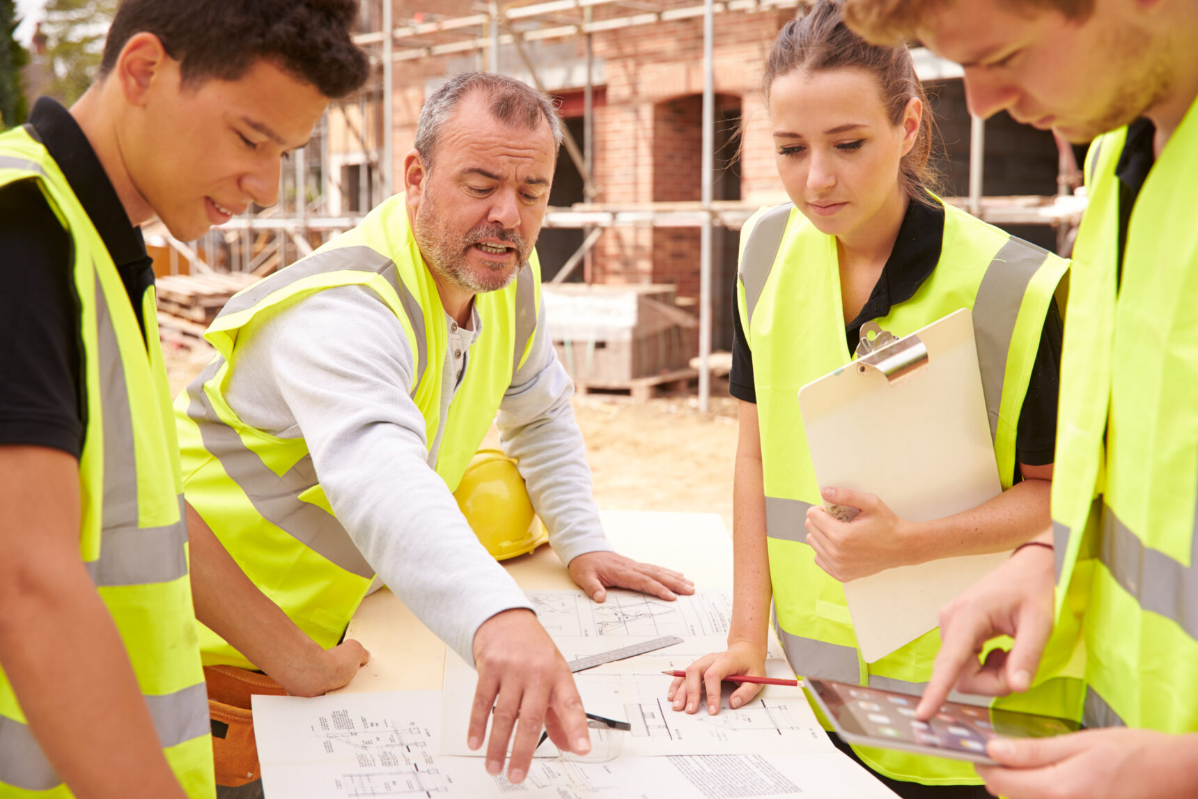 A tutor explains drawings to a group of students wearing high-vis vests who are studying a vocational building course.