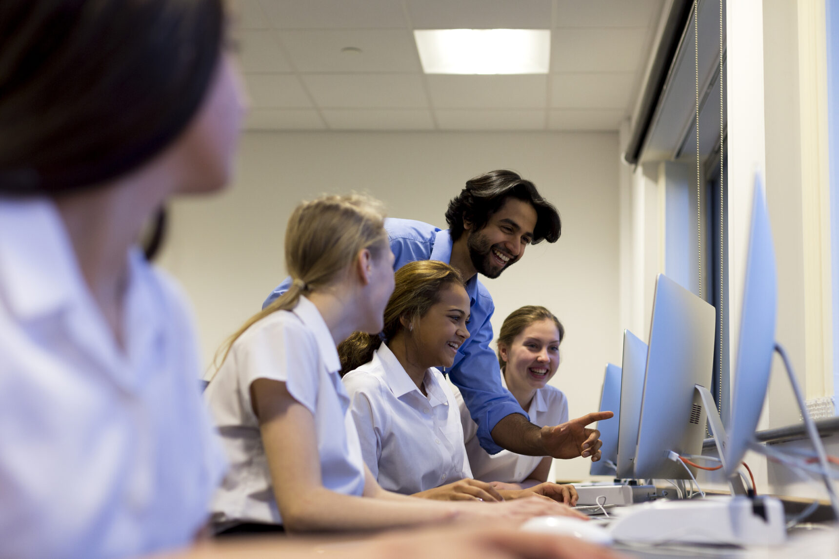 A male teacher laughing and smiling with a group of students. A positive classroom culture supports student resilience and well-being.