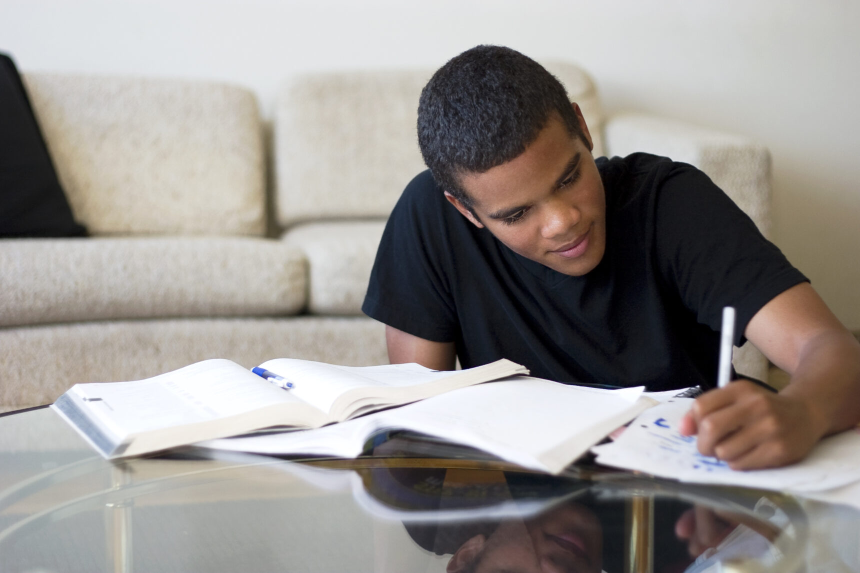 A teenage boy sits at a table surrounded by textbooks and papers highlighting notes as he prepares for the AQA GCSE Geography Paper 3 exam.