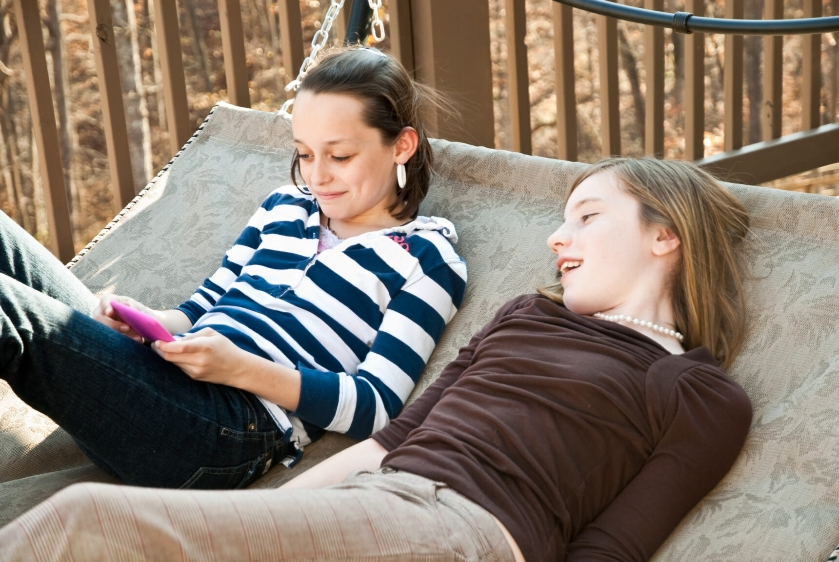 Two teenage girls are hanging out together on a garden hammock as they take a break from exam revision.