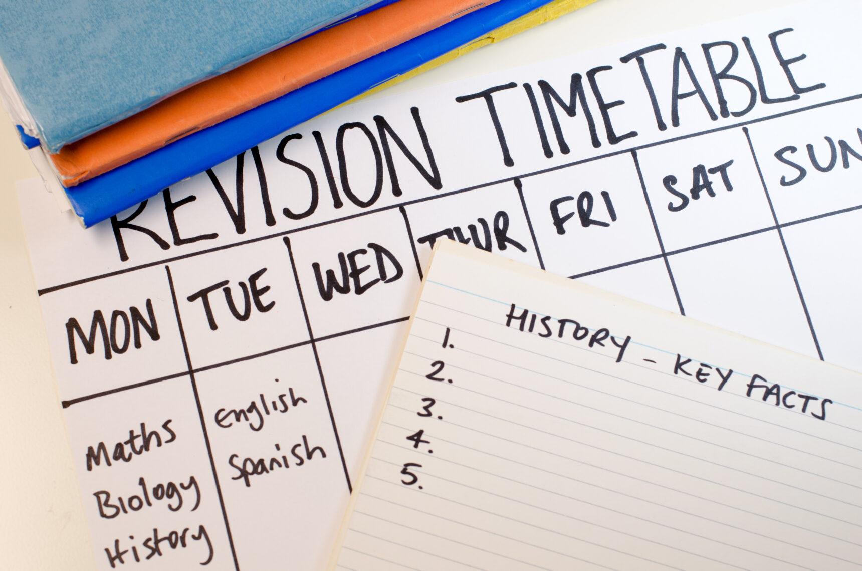 A hand-drawn revision timetable showing days of the week and a subject plan alongside the beginning of a handwritten flashcard for revising key history facts.