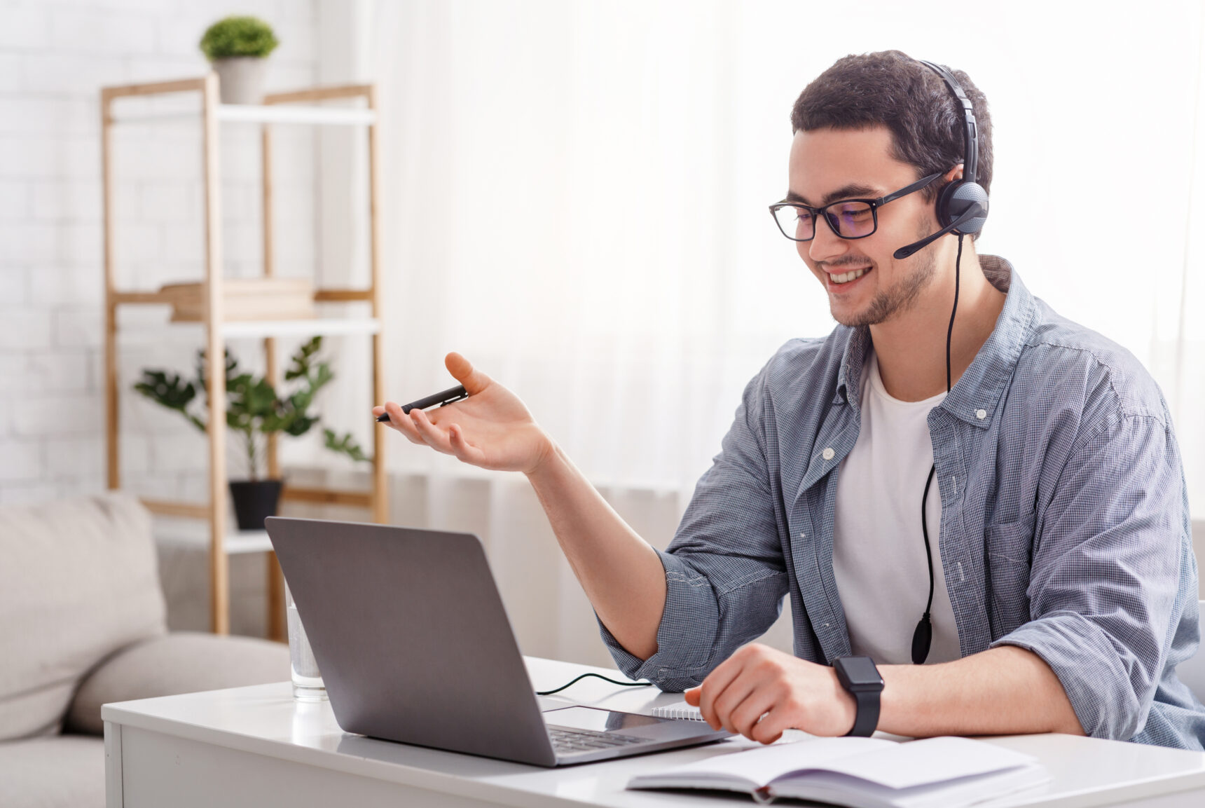 A male online tutor sitting at a desk wearing a headset delivering an engaging lesson to his student.