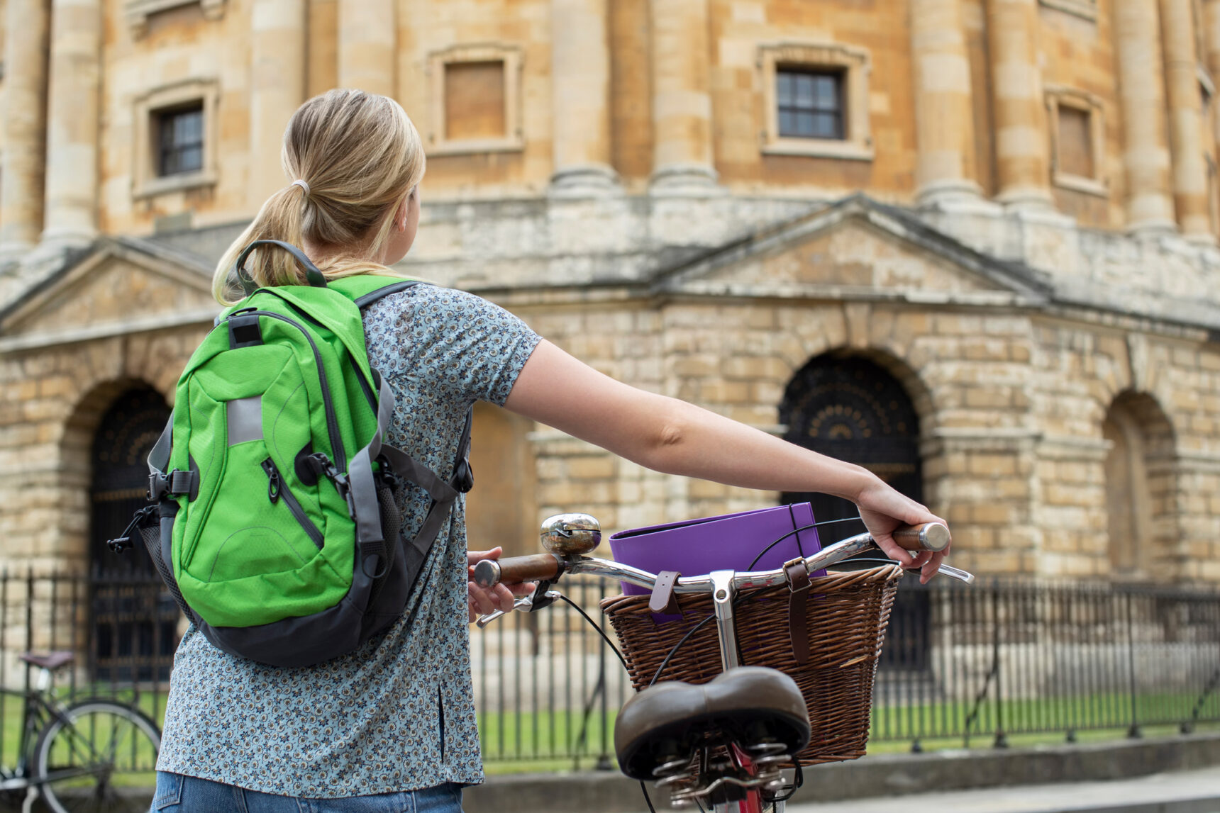 A student wearing a backpack arrives at Oxford University by bicycle.