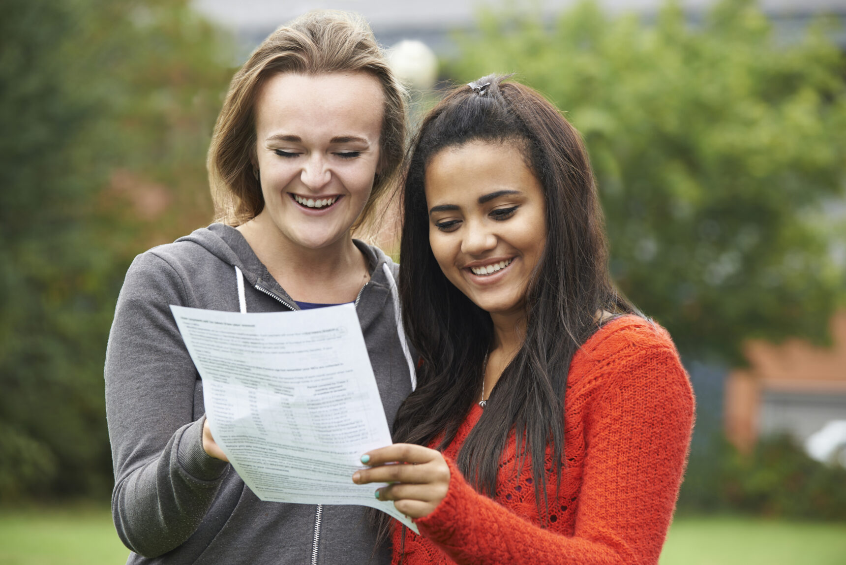Two female students stand outside their college smiling as they celebrate their A Level exam results.