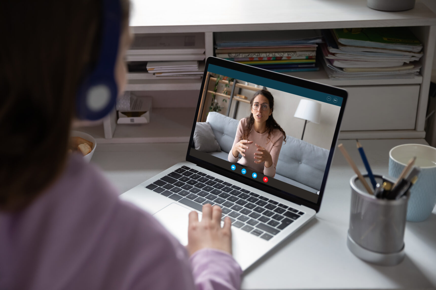 A teenage girl wearing a headset is receiving an online tutoring session from a female tutor.
