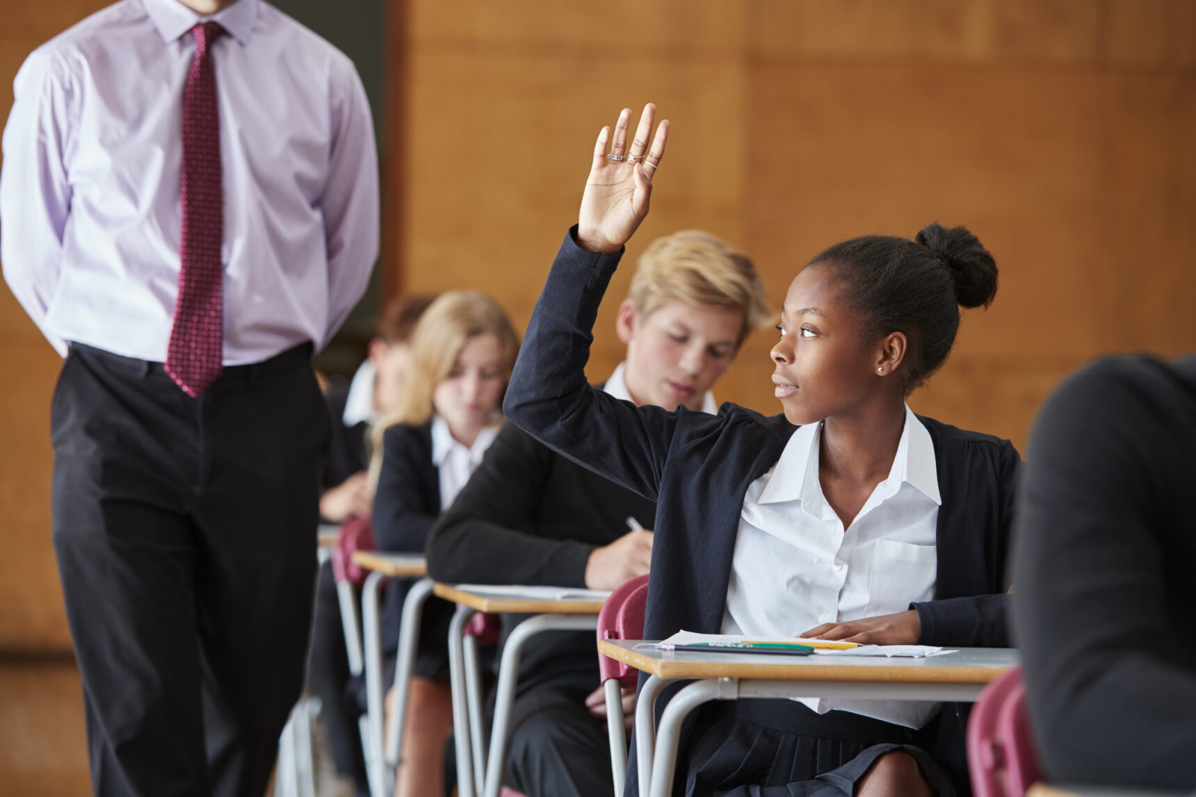 A female student raises her hand to ask a question to the invigilator during a GCSE exam.