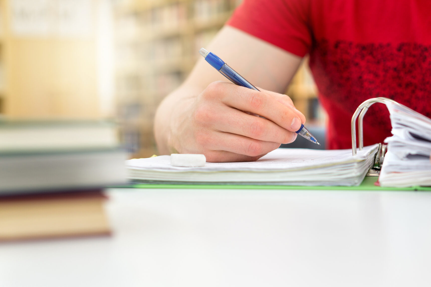 A GCSE student writes in a notebook surrounded by books as they prepare for their GCSE English Language exam.