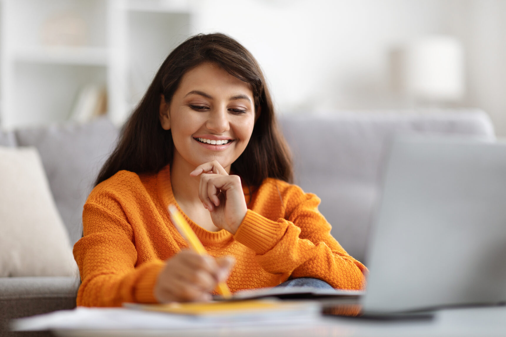 A teenage girl sits at a desk with a laptop smiling as she has recieved a positive GCSE remark outcome.