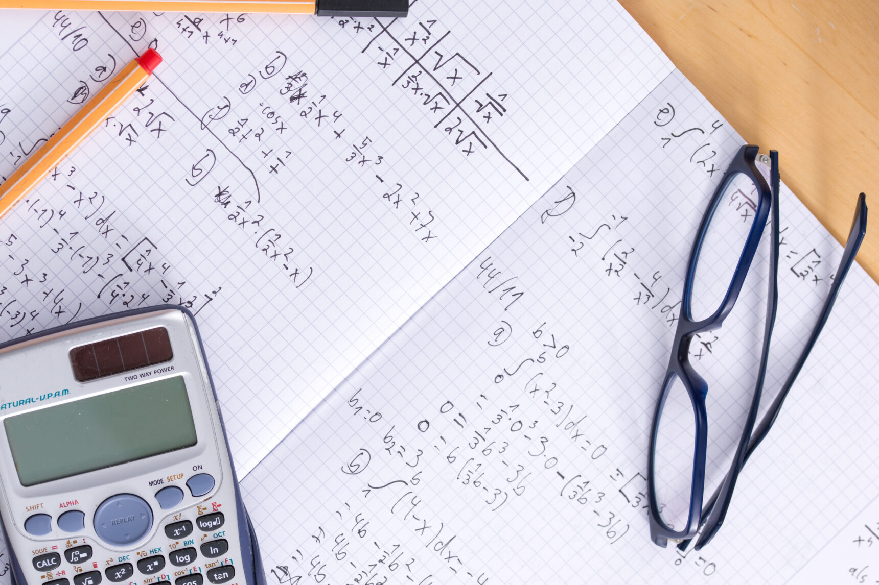 Close-up picture of a student's maths exercise book showing worked examples and a calculator.