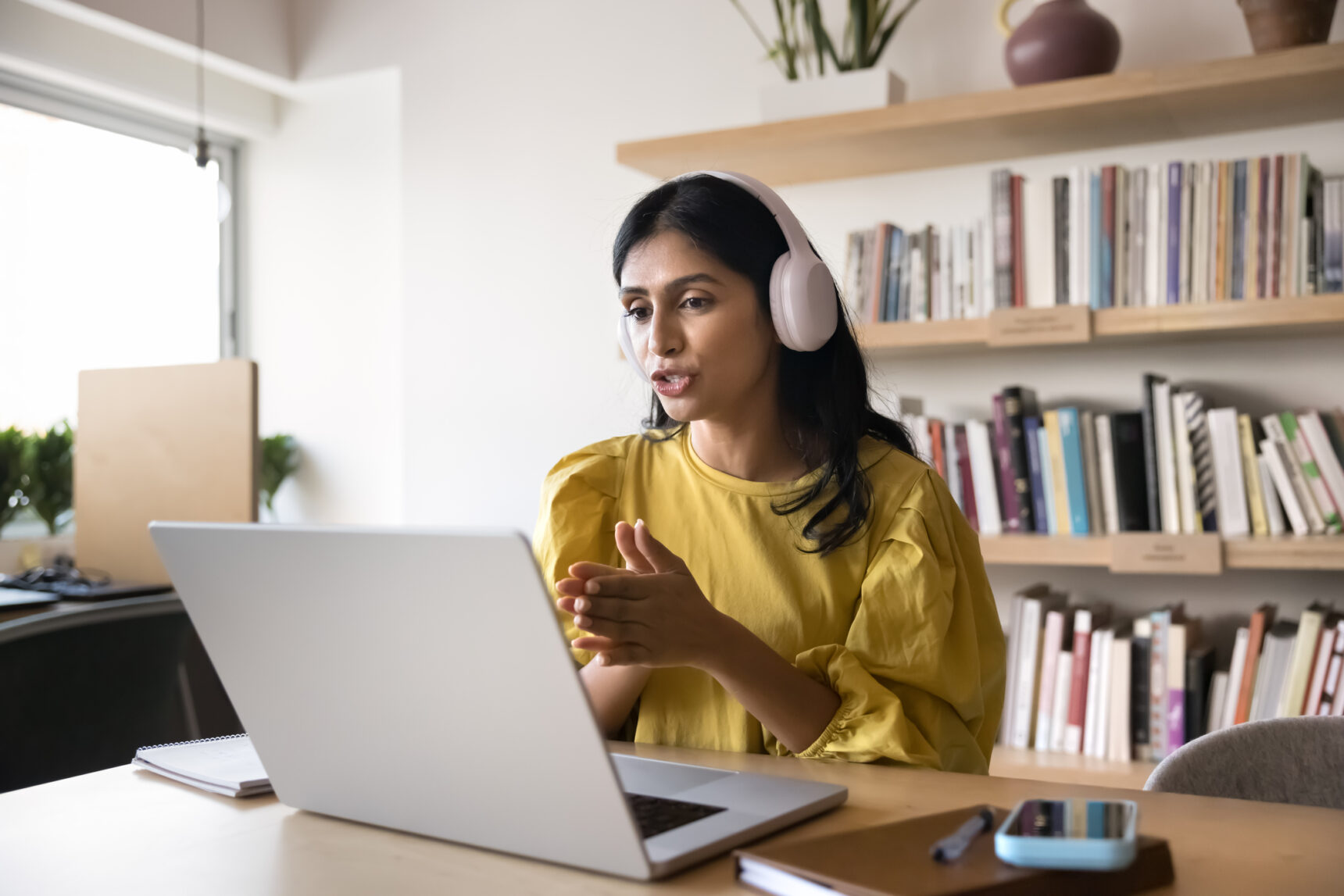 A female tutor wearing a headset is talking to a student during an online tutoring session.