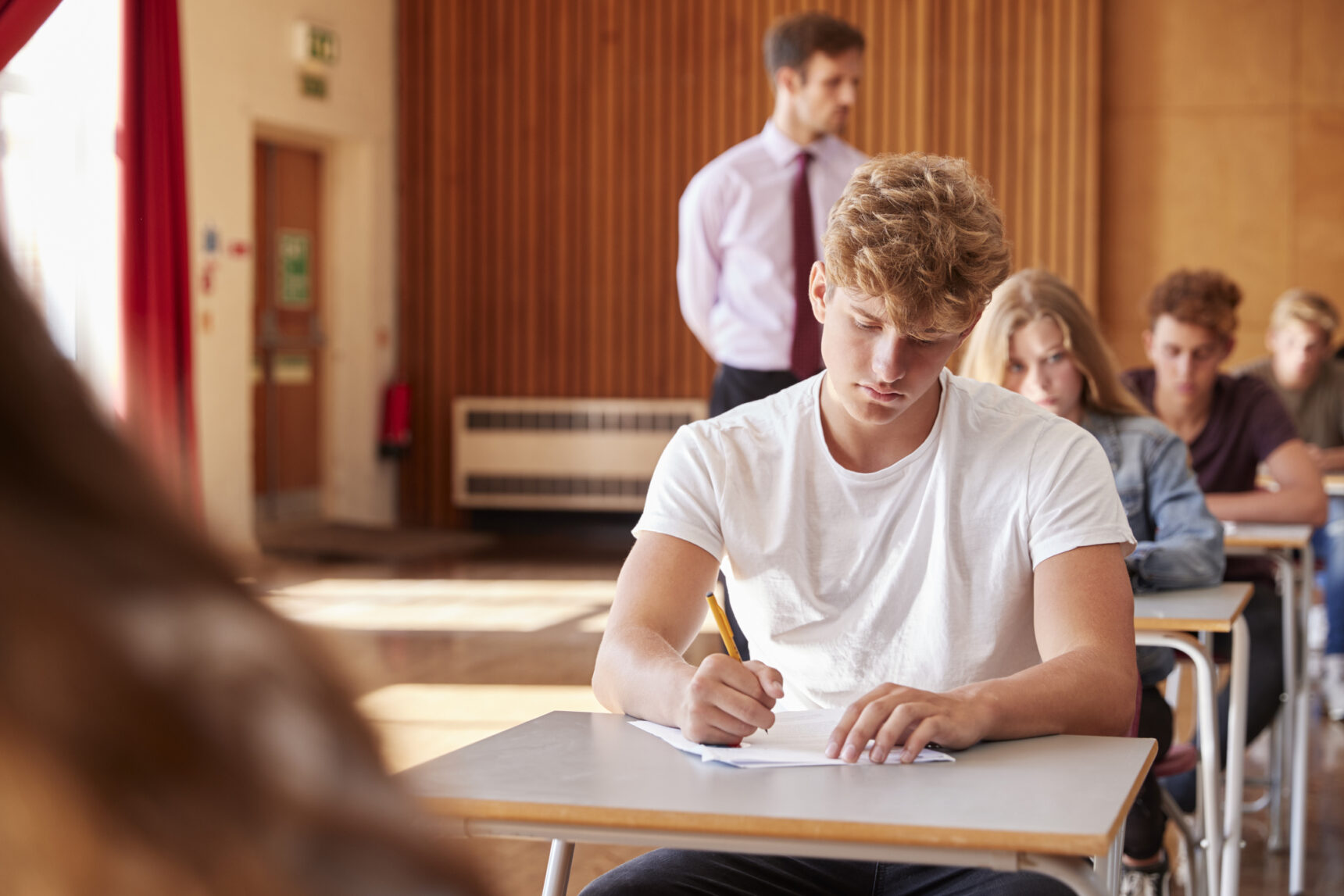 A group of GCSE students sitting the English Language exam in an exam hall.
