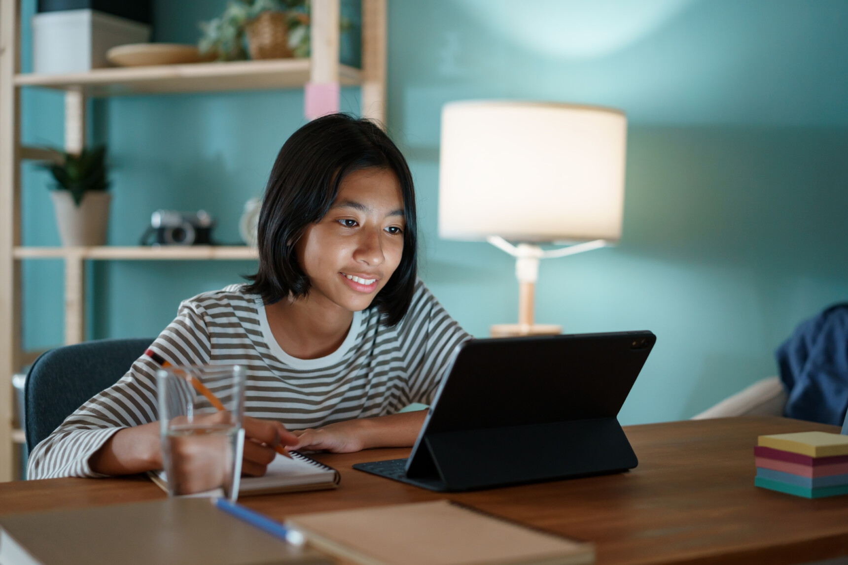 A female GCSE student is taking notes during an online English tutoring lesson.