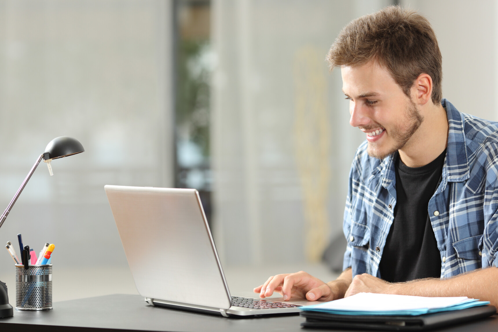 A male online English tutor sitting at a laptop is smiling as he talks to a student.
