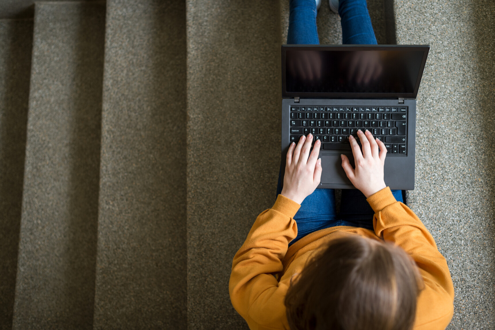 A student sitting on the floor researching university open days on a laptop.