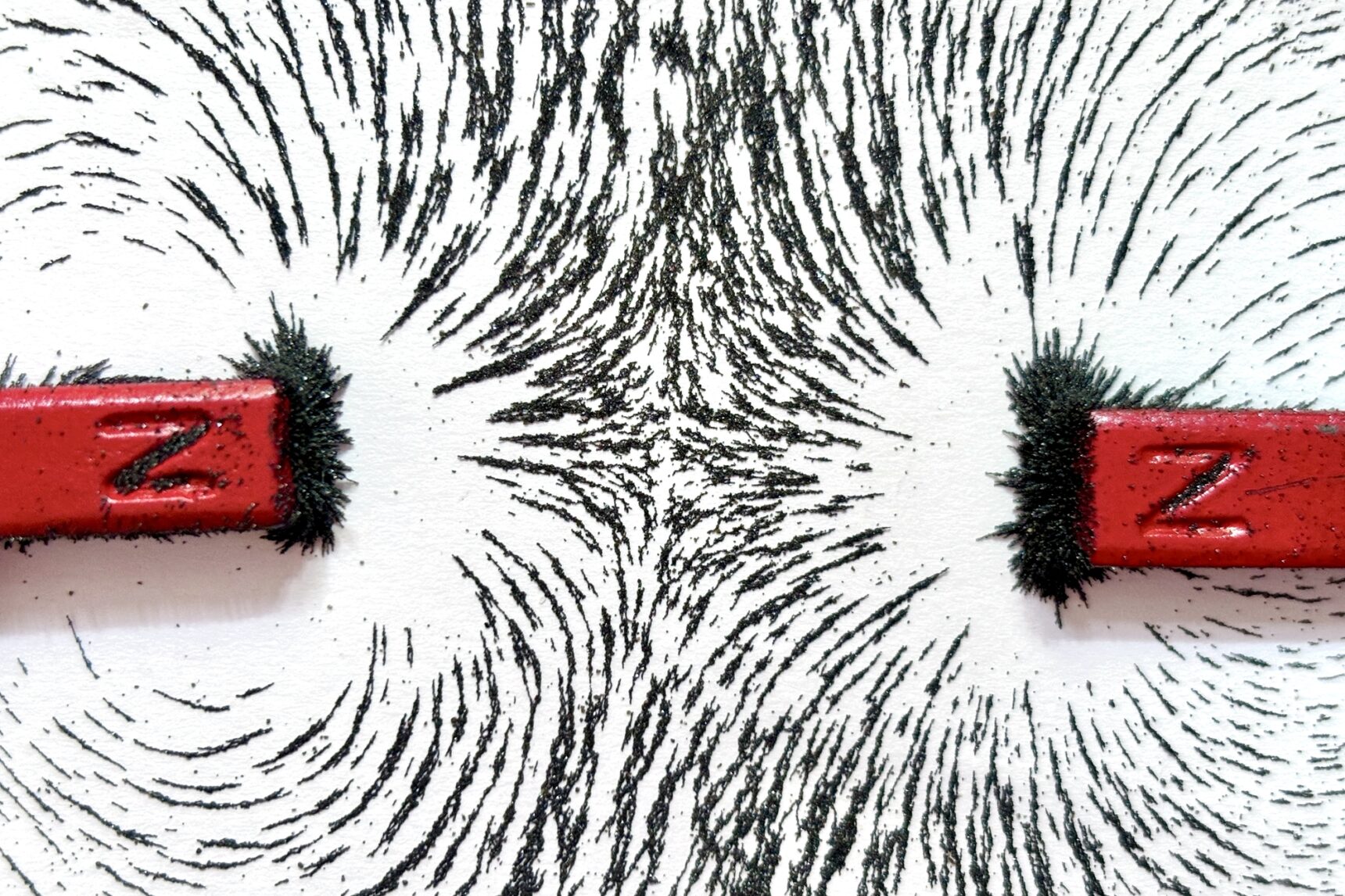 Two bar magnets are placed with opposite poles facing each other. Iron filings scattered on a white surface reveal the magnetic field lines.