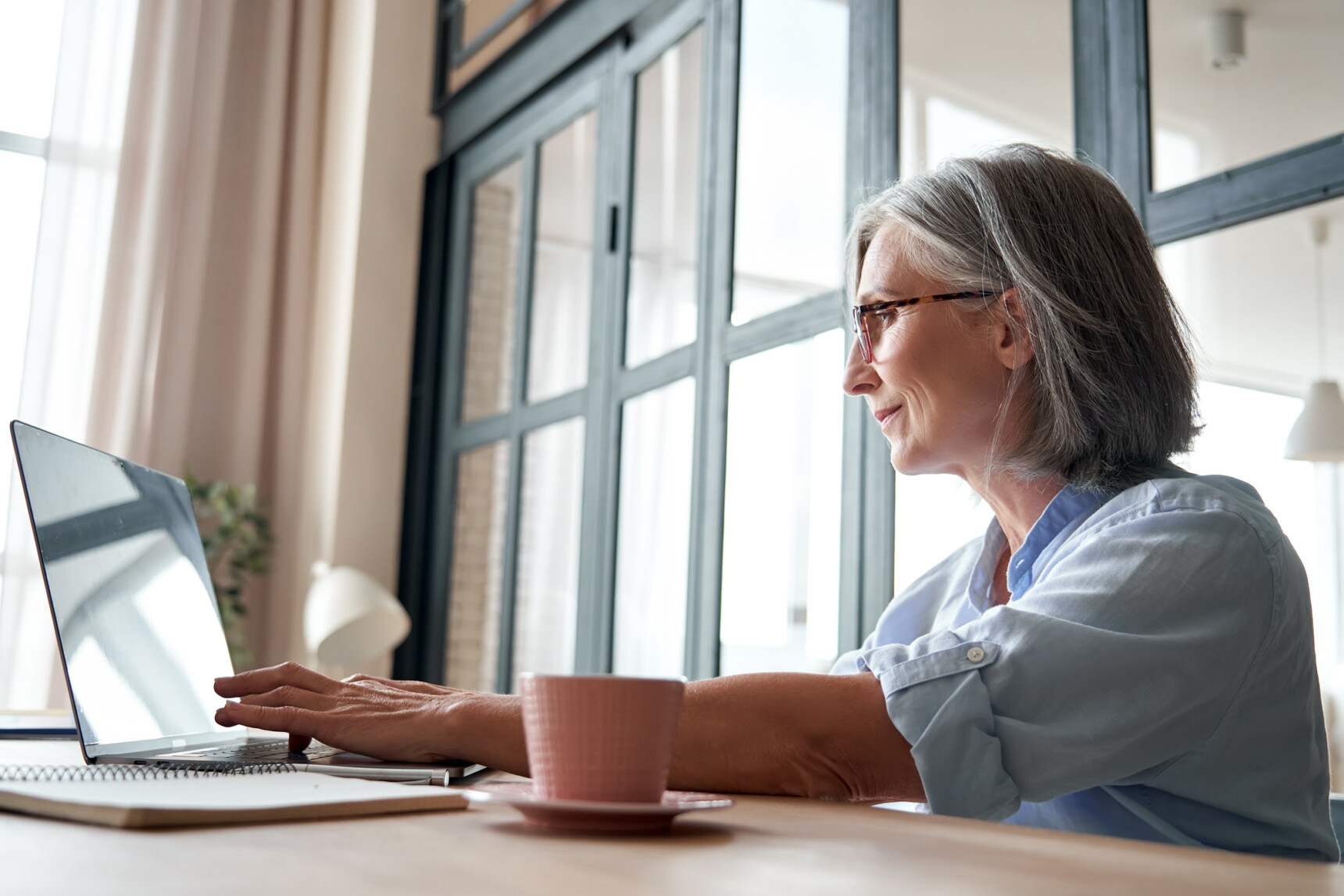 A retired female teacher working at a laptop, tutoring during her retirement.
