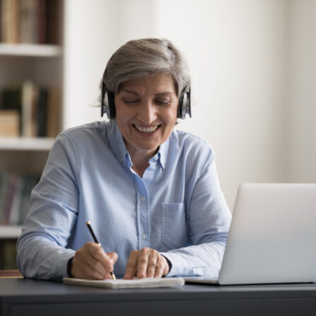 A retired female teacher is delivering an online tutoring session on a laptop.